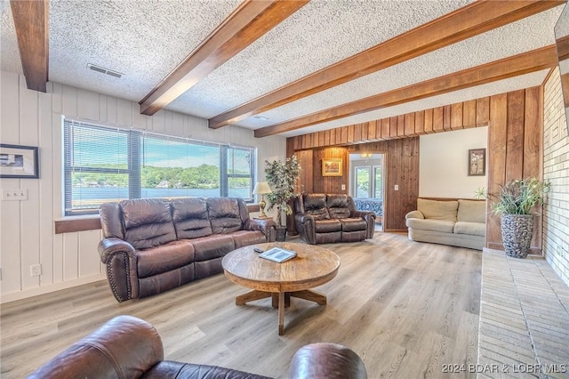 living area with visible vents, wooden walls, a textured ceiling, wood finished floors, and beamed ceiling