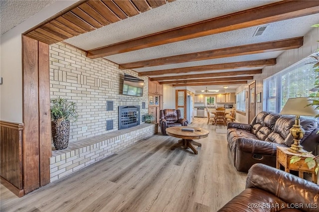 living room featuring light wood finished floors, a fireplace, a textured ceiling, and beamed ceiling