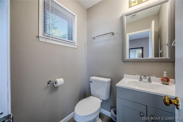 bathroom featuring baseboards, a textured wall, vanity, and toilet