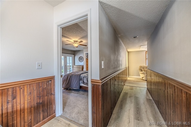 corridor with a textured ceiling, light hardwood / wood-style floors, and wooden walls