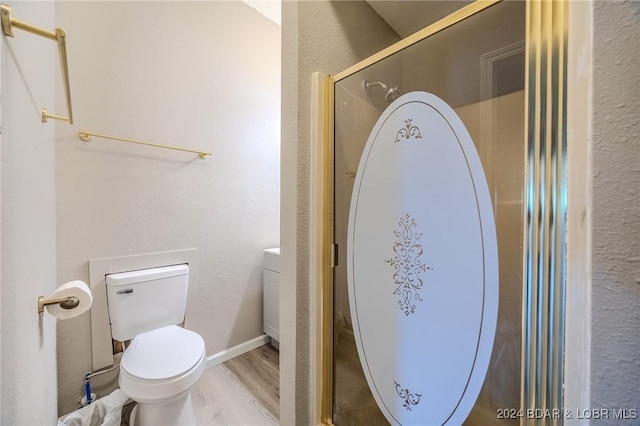 bathroom with a textured wall, toilet, wood finished floors, a shower with shower door, and vanity