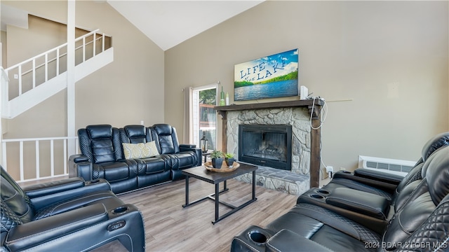 living room with a stone fireplace, high vaulted ceiling, and light wood-type flooring