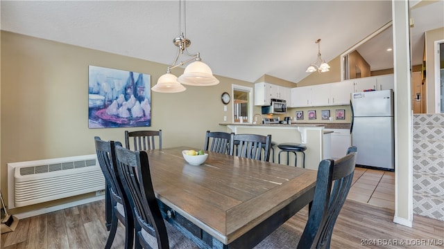 dining room with vaulted ceiling, light wood-type flooring, and a wall unit AC