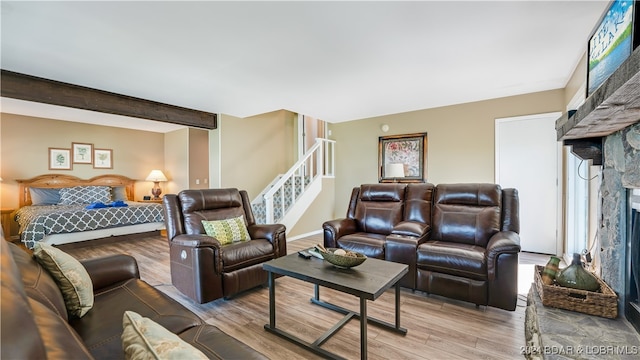 living room featuring light hardwood / wood-style floors, beam ceiling, a stone fireplace, and a wealth of natural light