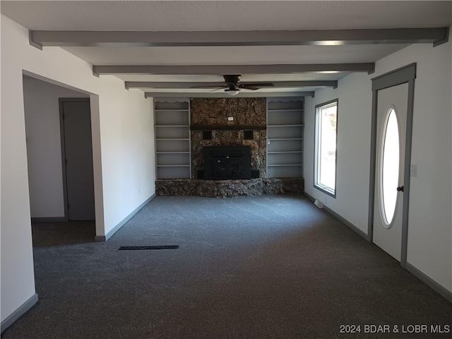 unfurnished living room featuring dark carpet, a stone fireplace, and ceiling fan