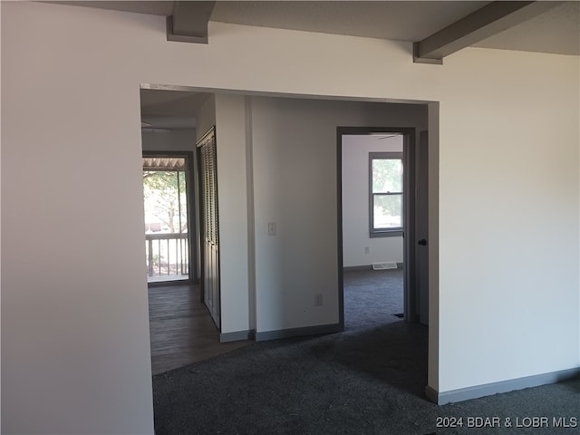 hall featuring beamed ceiling and dark carpet