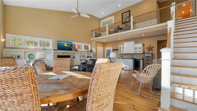 dining space with light wood-type flooring, a fireplace, ceiling fan, wine cooler, and high vaulted ceiling