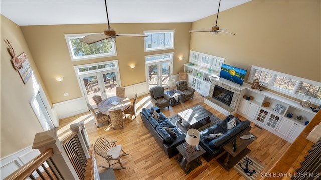 living room with light hardwood / wood-style floors, a fireplace, high vaulted ceiling, and ceiling fan