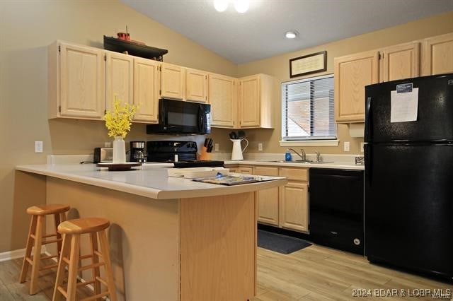 611 Lazy Days Rd Unit X11, Osage Beach, MO 65065 - kitchen with lofted ceiling, a kitchen bar, a sink, light wood-style flooring, and black appliances