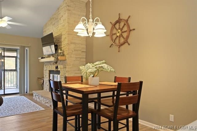 dining space featuring ceiling fan with notable chandelier, lofted ceiling, a fireplace, and hardwood / wood-style floors