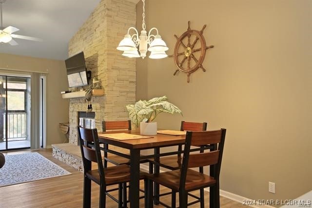 611 Lazy Days Rd Unit X11, Osage Beach, MO 65065 - dining space featuring a stone fireplace, wood finished floors, and ceiling fan with notable chandelier