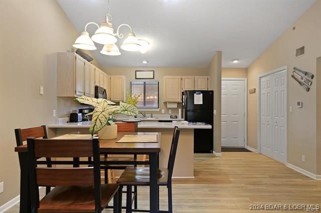 kitchen featuring light hardwood / wood-style flooring, hanging light fixtures, sink, black appliances, and vaulted ceiling