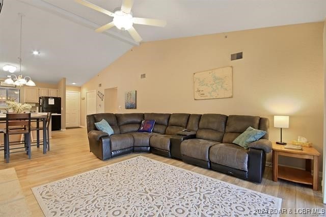 living room featuring vaulted ceiling, ceiling fan with notable chandelier, and light wood-type flooring