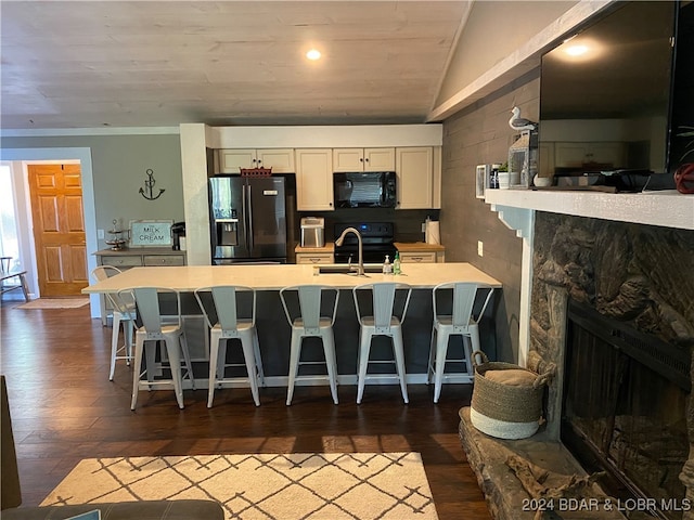 kitchen with black appliances, vaulted ceiling, a kitchen breakfast bar, and dark hardwood / wood-style floors