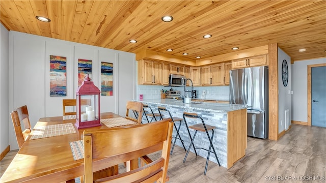 kitchen featuring decorative backsplash, light brown cabinets, stainless steel appliances, light stone countertops, and light wood-type flooring