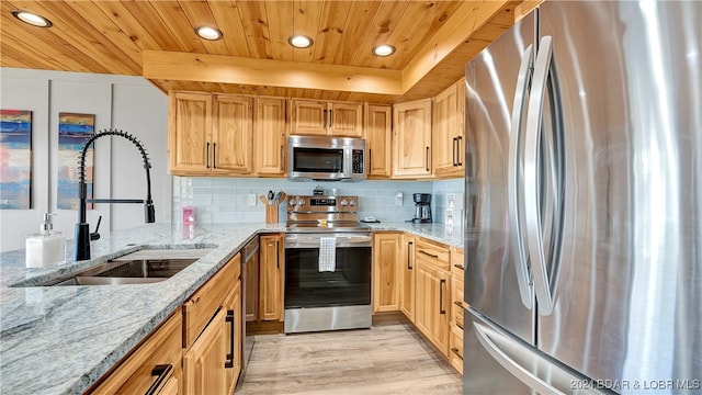 kitchen with sink, light stone countertops, appliances with stainless steel finishes, and light hardwood / wood-style flooring