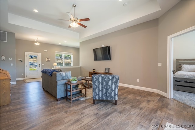 living room with dark hardwood / wood-style floors, a tray ceiling, and ceiling fan