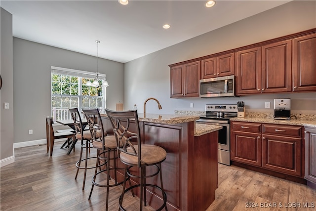 kitchen featuring appliances with stainless steel finishes, light hardwood / wood-style flooring, a kitchen island with sink, and decorative light fixtures