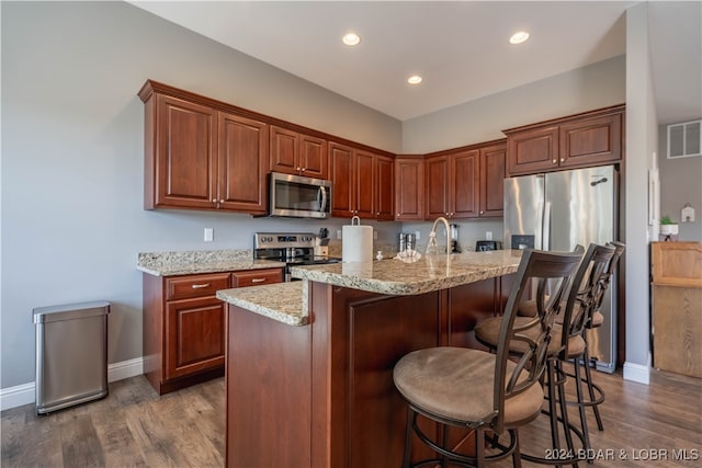 kitchen with dark hardwood / wood-style floors, a kitchen island with sink, and stainless steel appliances