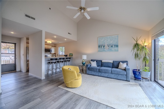 living room with a wealth of natural light, hardwood / wood-style flooring, high vaulted ceiling, and ceiling fan