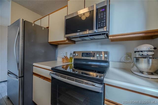 kitchen featuring a textured ceiling, white cabinetry, stainless steel appliances, and light wood-type flooring