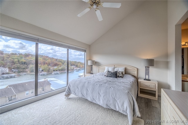 bedroom featuring access to exterior, hardwood / wood-style floors, a water view, high vaulted ceiling, and ceiling fan