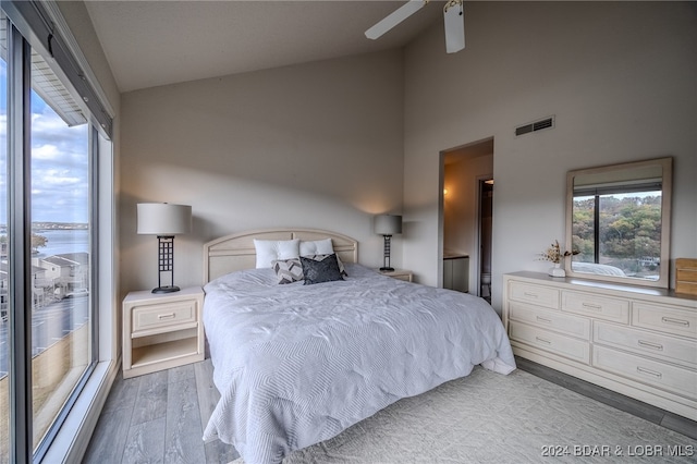 bedroom with a water view, ceiling fan, high vaulted ceiling, and light wood-type flooring