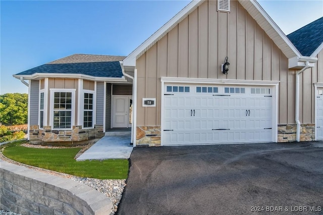 single story home with a garage, a shingled roof, stone siding, driveway, and board and batten siding