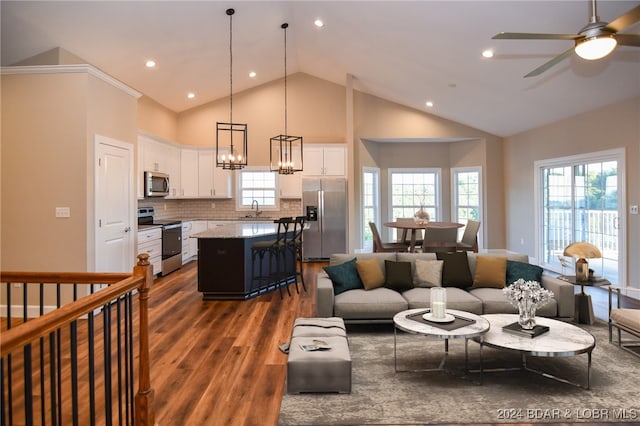 living area with ceiling fan with notable chandelier, high vaulted ceiling, dark wood finished floors, and recessed lighting