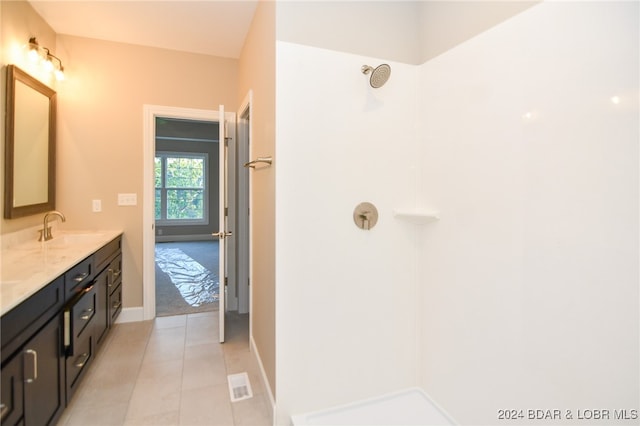 full bathroom with double vanity, baseboards, tile patterned floors, walk in shower, and a sink