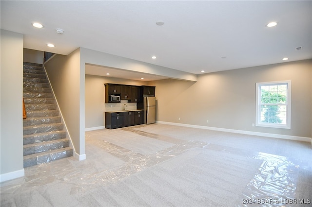 unfurnished living room with stairs, recessed lighting, a sink, and baseboards