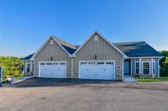 view of front facade with an attached garage, a shingled roof, stone siding, driveway, and board and batten siding