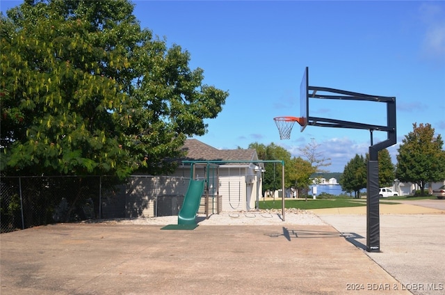 view of basketball court with basketball hoop, fence, and a playground