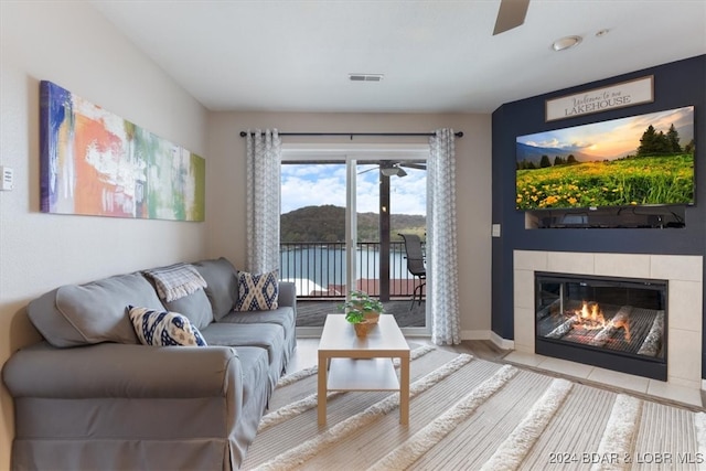 living room with light hardwood / wood-style flooring, a tiled fireplace, and ceiling fan