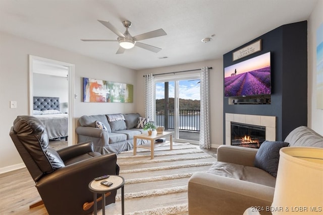 living room featuring hardwood / wood-style floors, a tiled fireplace, and ceiling fan