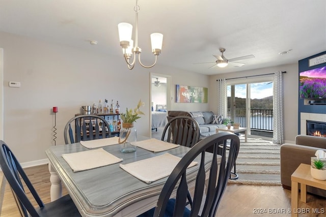 dining room with a tile fireplace, light hardwood / wood-style floors, and ceiling fan with notable chandelier