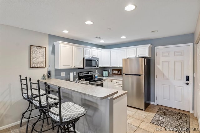 kitchen featuring kitchen peninsula, white cabinets, light tile patterned floors, a breakfast bar area, and stainless steel appliances