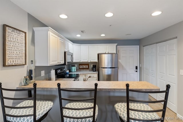 kitchen featuring kitchen peninsula, sink, white cabinets, a kitchen bar, and appliances with stainless steel finishes