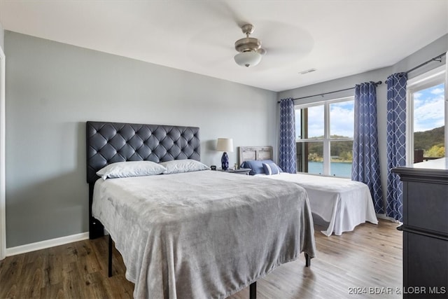 bedroom featuring wood-type flooring, a water view, and ceiling fan