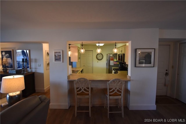 kitchen featuring dark wood-type flooring, a breakfast bar area, stainless steel refrigerator, kitchen peninsula, and pendant lighting