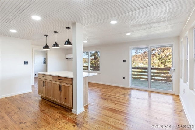 kitchen with an AC wall unit, a healthy amount of sunlight, light wood-type flooring, and hanging light fixtures