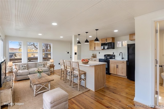 kitchen with light brown cabinetry, black appliances, light wood-type flooring, a center island, and decorative light fixtures