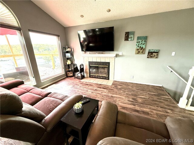 living room with a textured ceiling, a tile fireplace, wood-type flooring, and vaulted ceiling