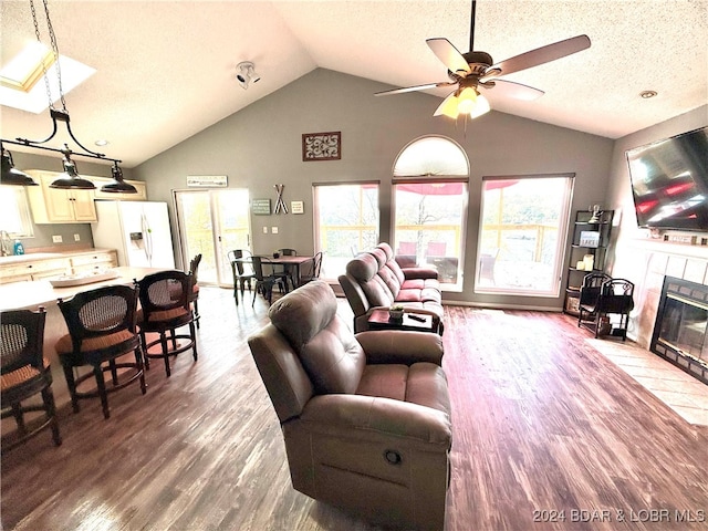 living room with vaulted ceiling, hardwood / wood-style flooring, ceiling fan, a textured ceiling, and a tiled fireplace