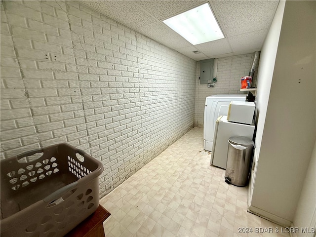 washroom featuring washing machine and dryer, electric panel, and brick wall