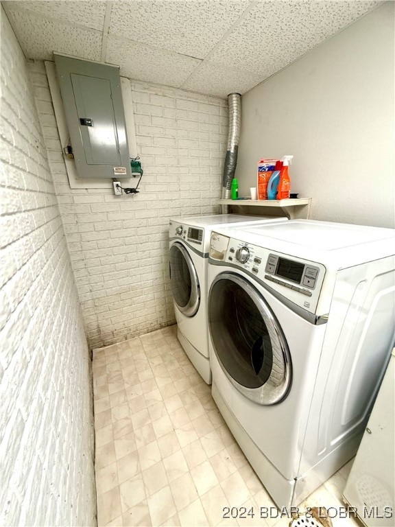 laundry area featuring brick wall, electric panel, and washing machine and clothes dryer