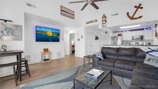 living room with ceiling fan, light hardwood / wood-style flooring, and a high ceiling