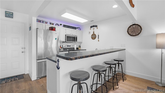 kitchen featuring a kitchen breakfast bar, stainless steel appliances, white cabinets, hardwood / wood-style floors, and kitchen peninsula