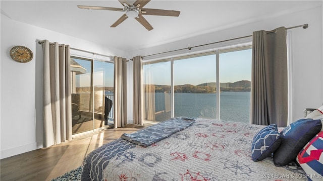 bedroom featuring hardwood / wood-style floors, a water view, ceiling fan, and access to exterior