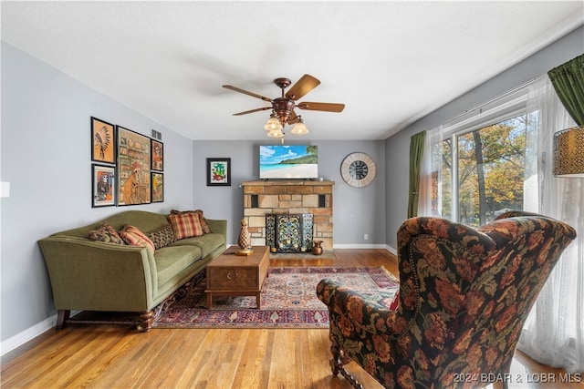 living room with a stone fireplace, wood-type flooring, and ceiling fan